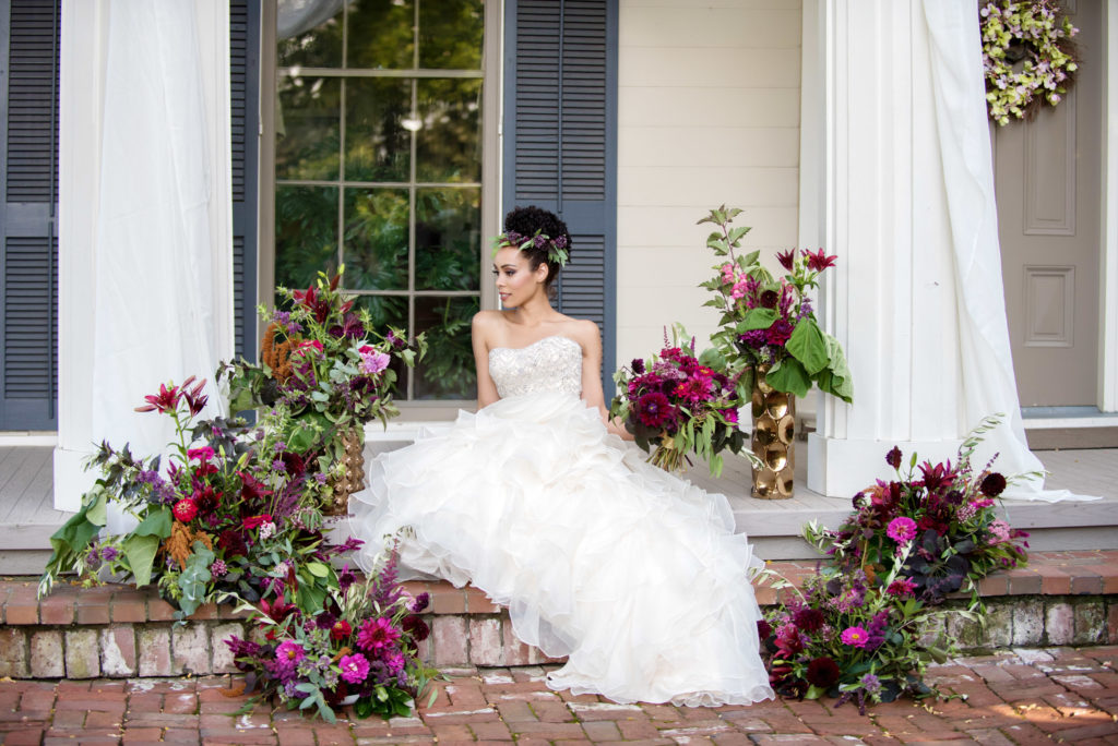 bride wearing ruffled wedding dress surrounded by purple and magenta bouquets