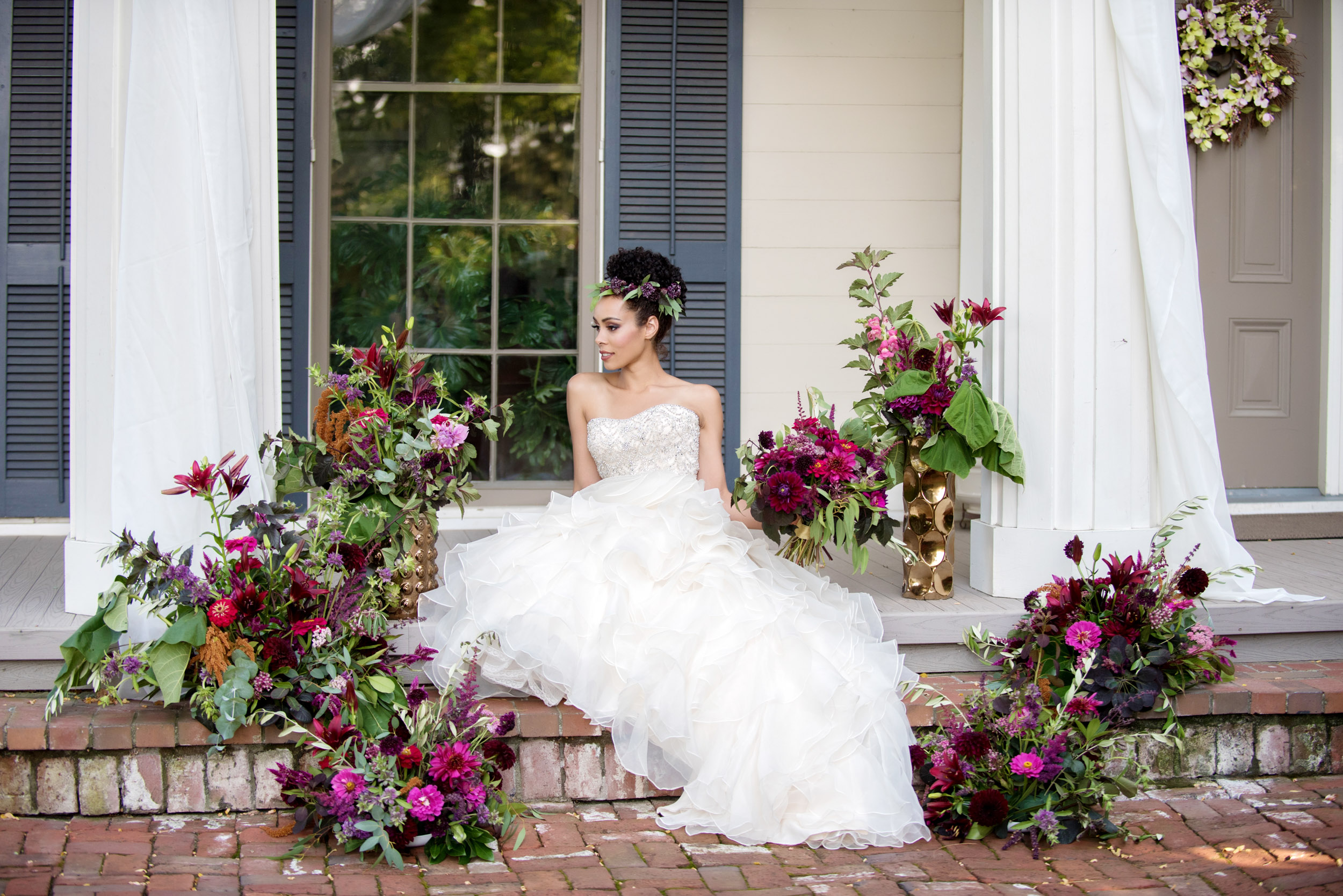 bride sits on steps of ainsworth house surrounded by purple and magenta bouquets