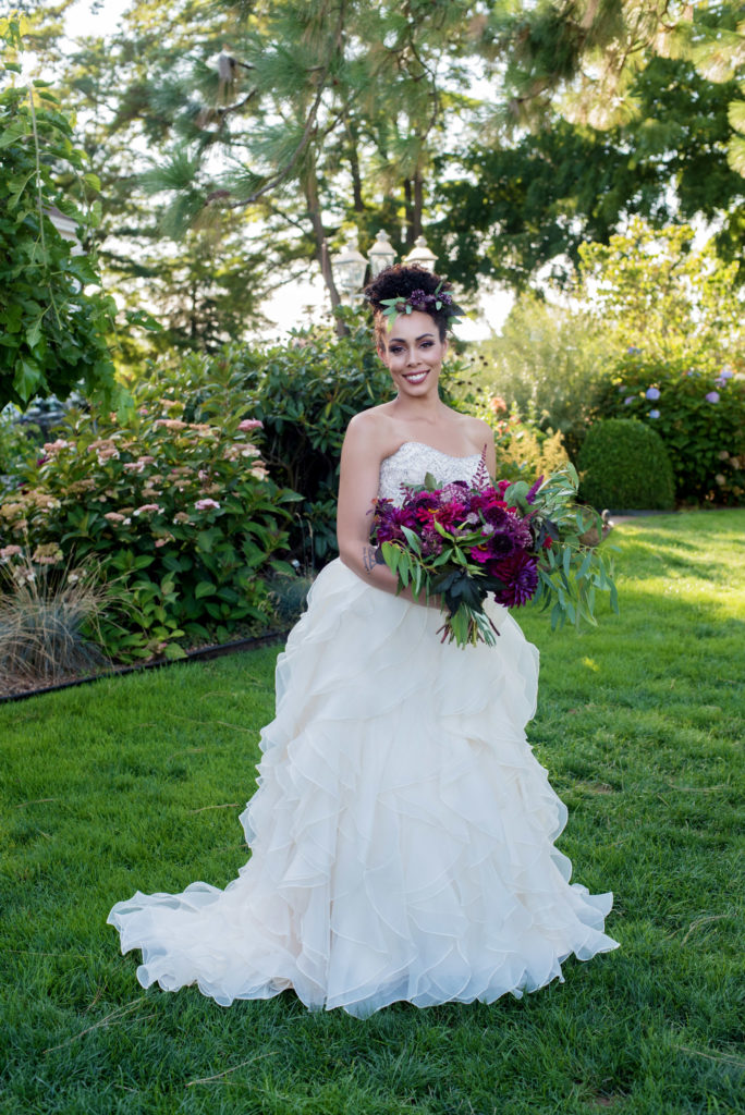 bride wearing ruffled wedding dress with purple and magenta bouquet