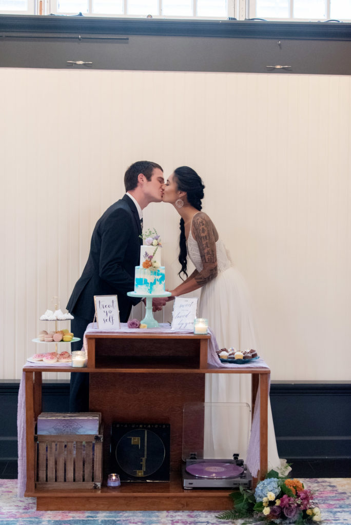 bride and groom kiss in front of a pastel watercolor cake by bees cakes at the evergreen pdx