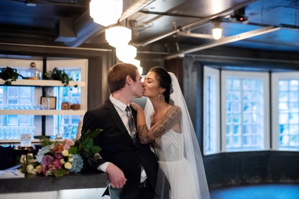 bride and groom lean on the bar and kiss at the evergreen pdx