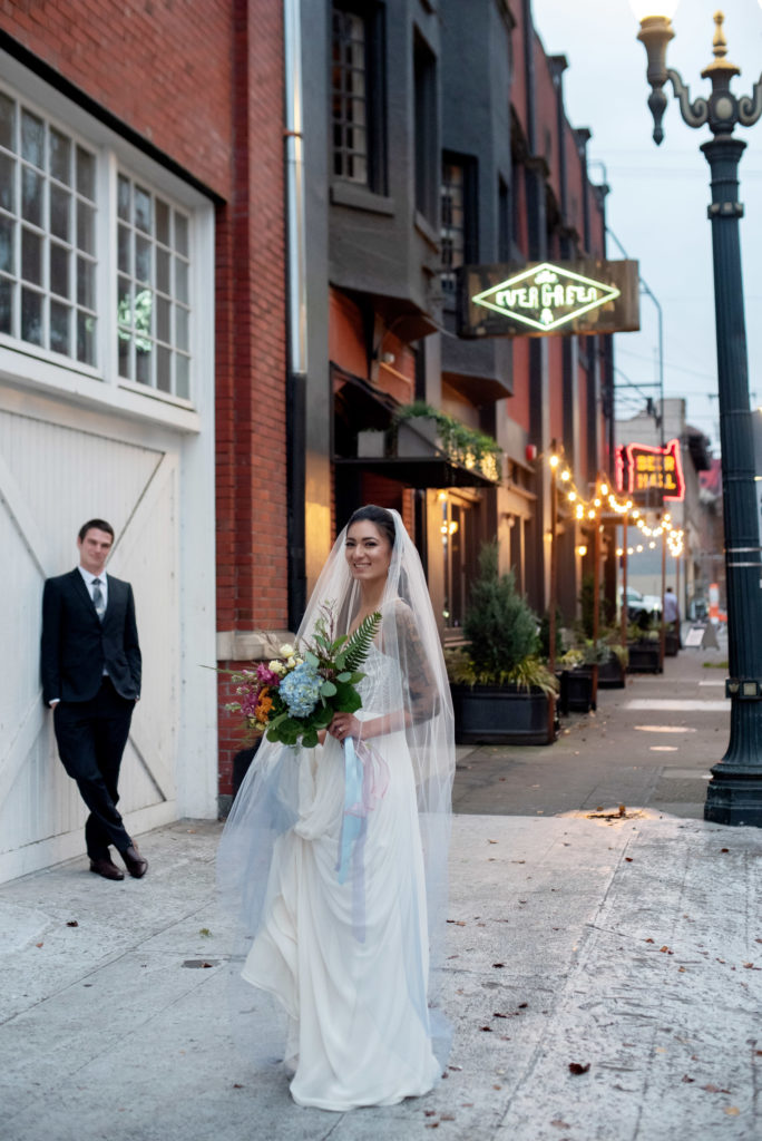 bride and groom outside of the evergreen pdx in central se portland, holding a pastel bouquet and wearing a vneck wedding dress and blue ombre veil