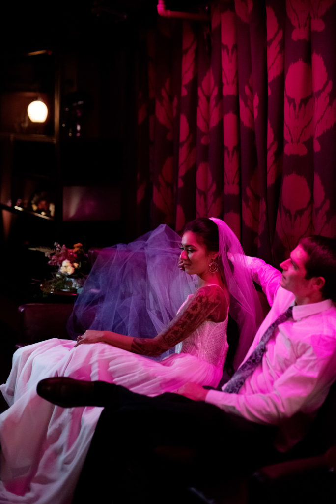 bride and groom lounge in the red lights of Voysey speakeasy
