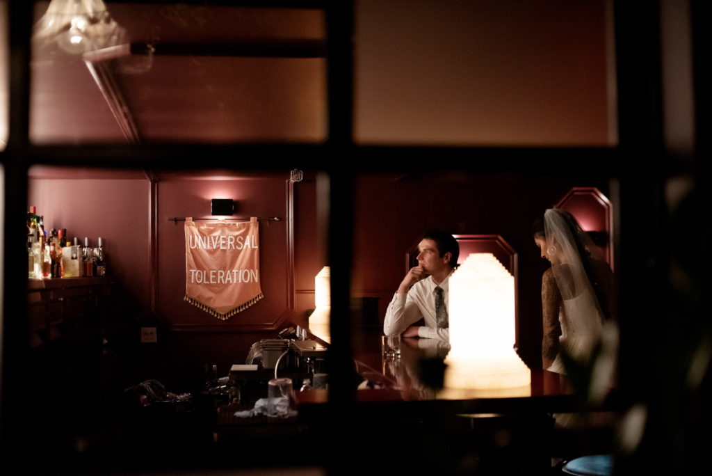 bride and groom sit at the bar at Voysey speakeasy bar