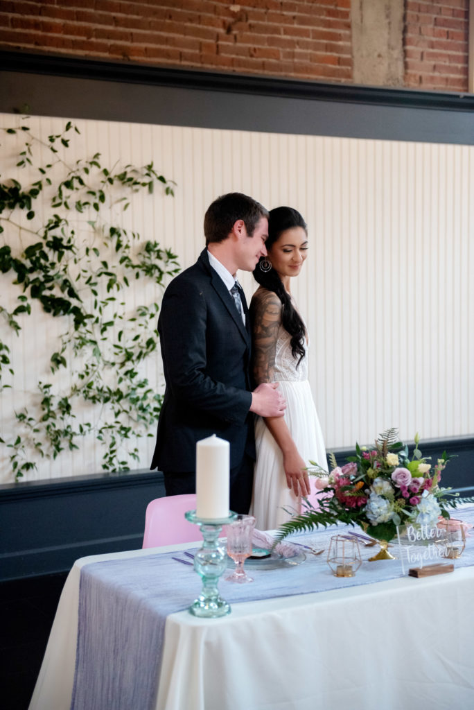 bride and groom by the pastel colored sweetheart table with bouquet by lush floral design