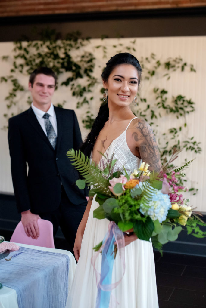 bride in low cut v-neck wedding dress and fishtail braid holds a pastel bridal bouquet 
